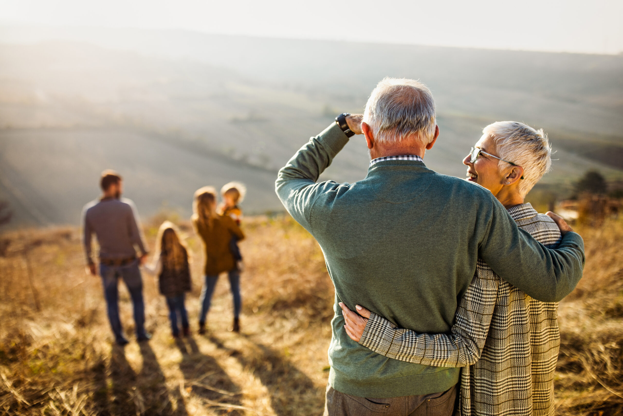 Rear view of Grandparents with children and grandchildren in a field, enjoying their Generational wealth.